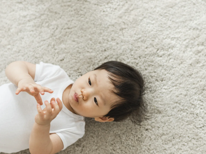baby laying on carpet playing with their fingers